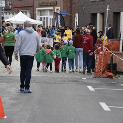 Gruppe von Kindern in grünen T-Shirts geht eine Straße entlang, begleitet von mehreren Zuschauern und Absperrungen.