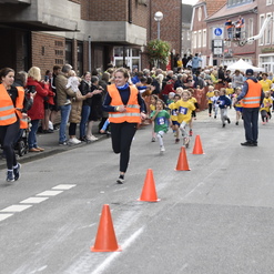 Kinderrennen auf einer Straße, mit Läufern in bunten Trikots und Zuschauern, die an der Strecke applaudieren.