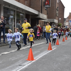 Kinder in Wettkampfkleidung laufen an Zuschauern vorbei, während eine Veranstaltung auf der Straße stattfindet.