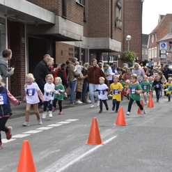 Gruppe von Kindern in Laufkleidung nimmt an einem Straßenlauf teil, umgeben von Zuschauern und Absperrungen.