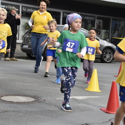 Kinder in gelben und grünen Shirts laufen beim Wettbewerb, umgeben von Zuschauern und gelben Absperrkegeln.
