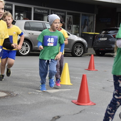 Kinder in Laufshirts nehmen an einem Wettlauf teil, während Verkehrshütchen auf dem Weg stehen.