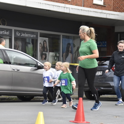 Kinder und Erwachsene laufen vor einem Friseursalon, gekennzeichnet durch bunte Startnummern und Verkehrscones.