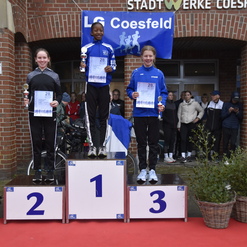 Drei Siegerinnen stehen auf dem Treppchen bei einer Sportveranstaltung, begleitet von Pokalen und Urkunden.