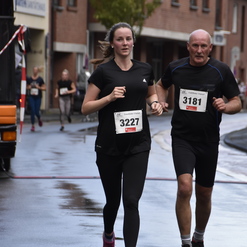 Zwei Läufer, eine Frau in Schwarz und ein Mann in Schwarz, joggen auf einer nassen Straße während eines Wettlaufs.