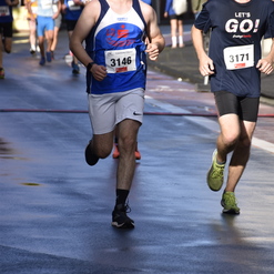 Zwei Läufer nehmen an einem Wettkampf teil, einer trägt ein blaues Trikot, der andere ein schwarzes T-Shirt mit Aufdruck.