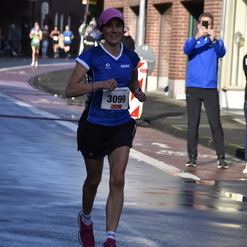 Läuferin mit Nummer 3099 in blauer Sportbekleidung joggt auf einer nassen Straße während eines Ereignisses.