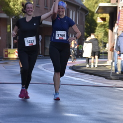 Zwei Frauen jubilieren beim Überqueren der Ziellinie eines Straßenlaufs, Hände erhoben und lächelnd.
