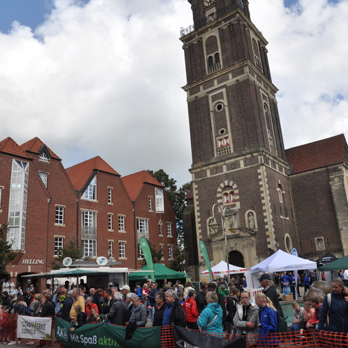 Belebte Stra&szlig;enansicht mit Menschenmenge und historischer Kirche im Hintergrund, umgeben von festlicher Atmosph&auml;re und St&auml;nden.