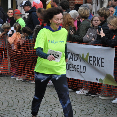 Läuferin in neongrünem Shirt mit der Startnummer 622 joggt vorbei, umgeben von Zuschauern an einer Keramikstraße.