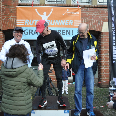 Sieger erh&auml;lt Gl&uuml;ckw&uuml;nsche auf der B&uuml;hne eines Sportevents, umgeben von Zuschauern und Teilnehmern.