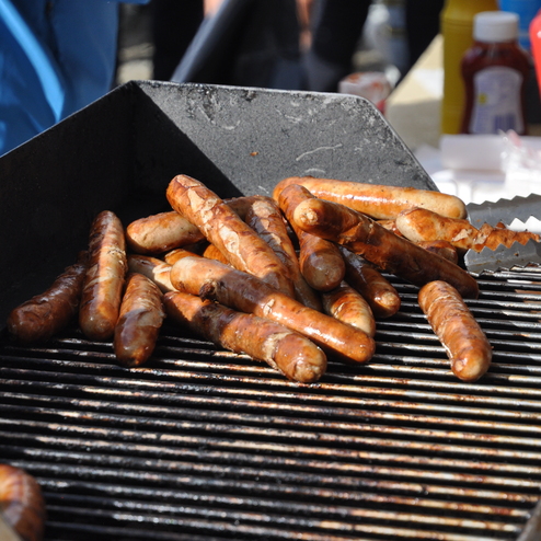 Grill mit mehreren gegrillten W&uuml;rstchen, umgeben von Zange und anderen Grillutensilien.