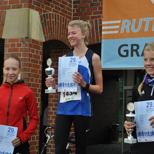 Drei junge L&auml;uferinnen stehen auf dem Podium, halten Pokale und Urkunden des 29. Coesfelder DJK Citylaufs.
