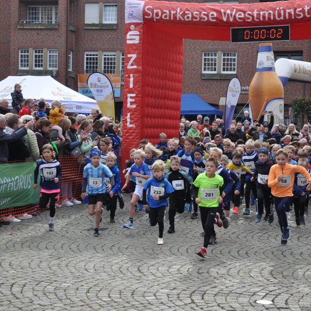 Start eines Kinderlaufs mit vielen jungen Teilnehmern, Publikumsbereich und einem großen Zielbogen im Hintergrund.