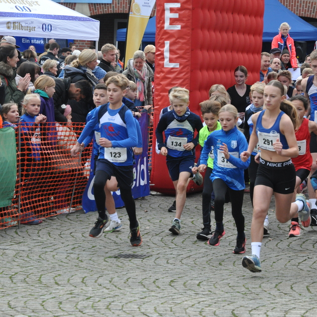 Kinder beim Start eines Laufwettbewerbs, umringt von Zuschauern an einem gepflasterten Platz.