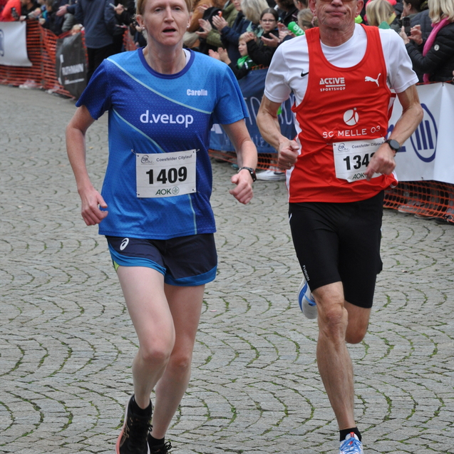 Zwei L&auml;ufer in sportlicher Kleidung laufen auf einer von Zuschauern ges&auml;umten Stra&szlig;e w&auml;hrend eines Wettkampfs.