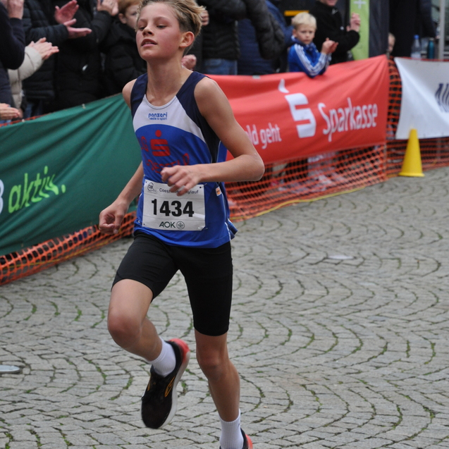 Ein junger L&auml;ufer mit Startnummer 1434 sprintet auf einer von Zuschauern ges&auml;umten Stra&szlig;e w&auml;hrend eines Wettkampfs.