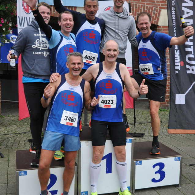 Gruppe von L&auml;ufern posiert auf dem Siegerpodest nach einem Wettkampf, alle in blauen Sporttrikots.