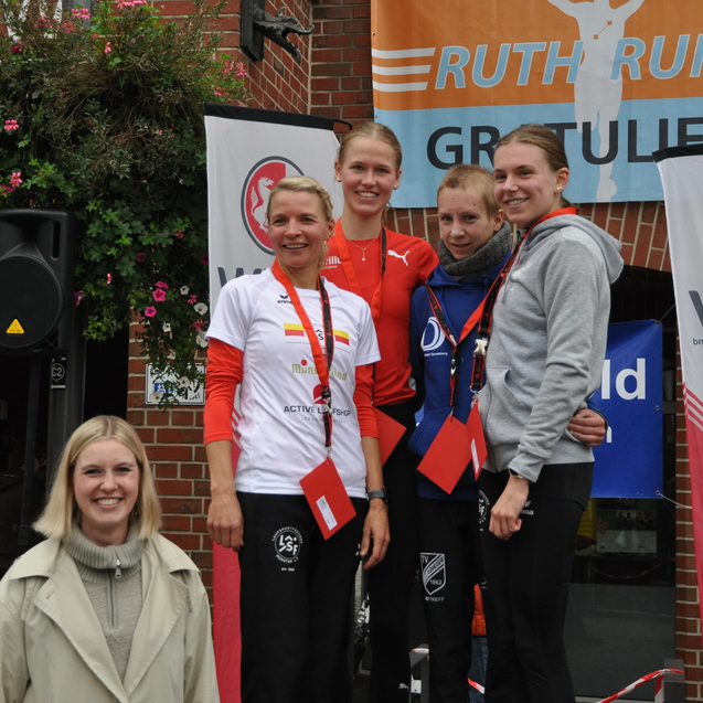 Gruppenszene von f&uuml;nf Personen, die auf einer Siegerehrung nach einem Laufwettbewerb stehen, mit Medaillen und Urkunden.