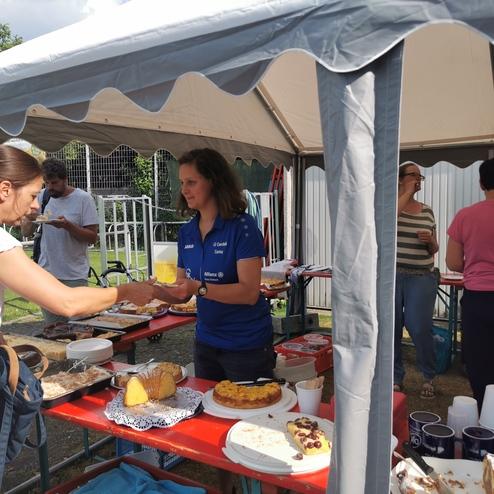 Menschen stehen an einem Tisch, um Speisen auszuwählen und sich zu unterhalten, während Kuchen und Snacks bereitstehen.