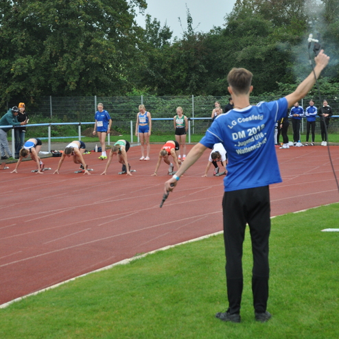 Startschuss für einen Sprintwettkampf: Athleten in der Startposition, Schiedsrichter mit Pistole am Rande der Laufbahn.