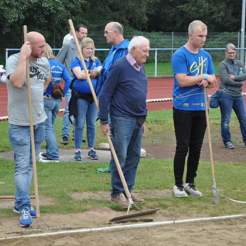 Gruppe von Menschen mit Schaufeln auf einer Sportanlage, beobachten einen Wettkampf im Weitsprung.