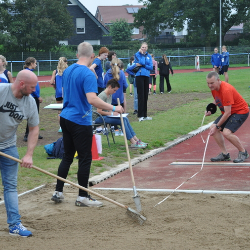 Gruppierung von Sportlern und Helfern bei der Vorbereitung eines Sandbereichs für einen Wettkampf auf einer Sportanlage.