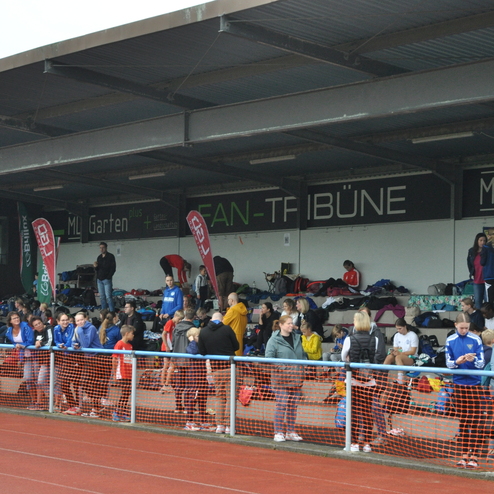 Gruppe von athletischen Zuschauern an einer Tribüne mit bunten Fanutensilien und Sporttaschen im Hintergrund.