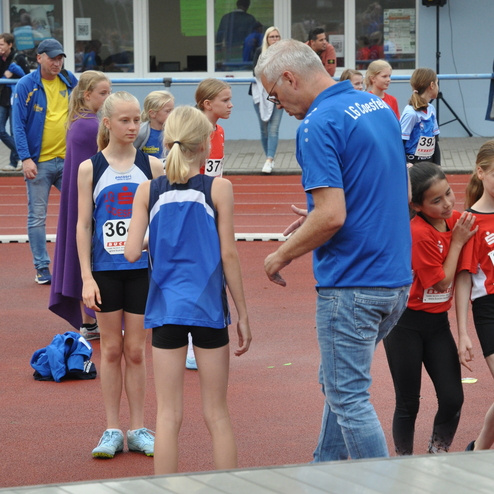 Gruppe junger Leichtathleten in Wettkampfsituation, Trainer erklärt den Teilnehmerinnen die Abläufe auf der Laufbahn.