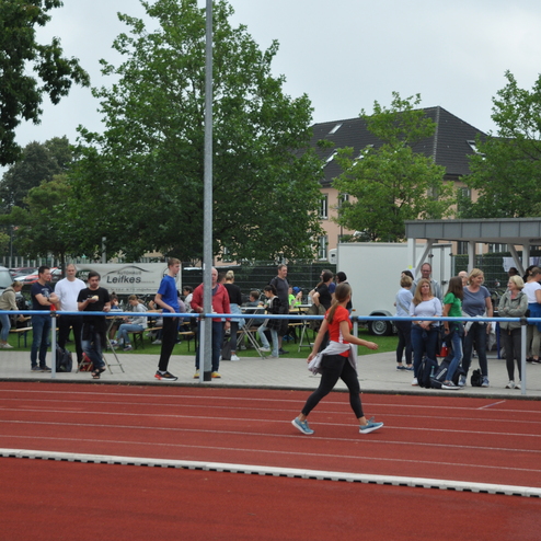 Sportveranstaltung auf einer roten Laufbahn mit Zuschauern und Teilnehmern in der Kulisse eines Stadions.