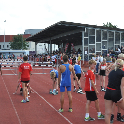 Jugendliche Athleten auf einer Laufbahn bereiten sich auf einen Wettkampf vor, Zuschauer sind auf der Trib&uuml;ne.
