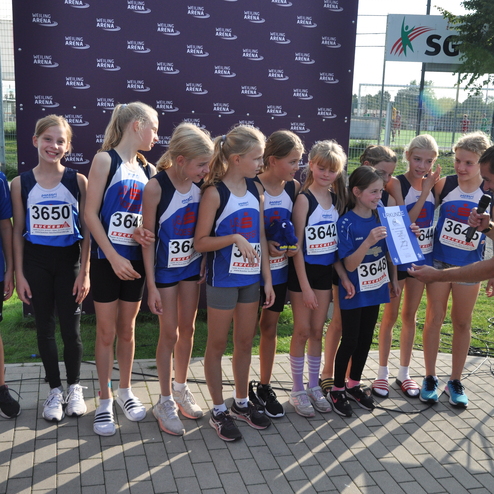 Gruppe junger Athletinnen zeigt stolz ihre Urkunde bei einer Sportveranstaltung im Freien.