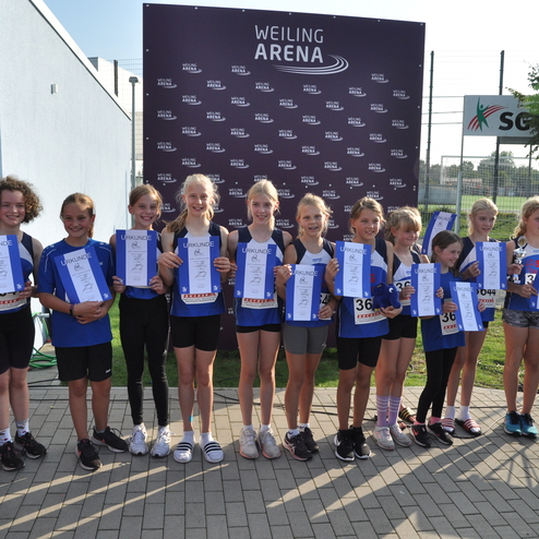 Gruppe von M&auml;dchen mit Urkunden, l&auml;chelnd vor einem Banner der Weiling Arena, in sportlicher Kleidung am Wettkampfort.
