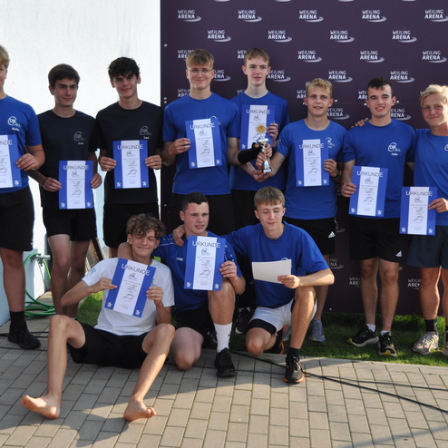 Gruppe von Jugendlichen in blauen T-Shirts h&auml;lt Urkunden und Pokale, posiert vor einer Wand mit &bdquo;Weiling Arena&ldquo;-Schriftzug.