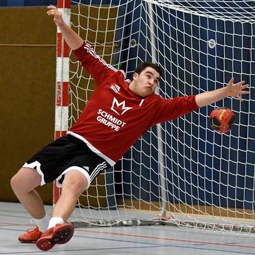 Handballtorwart in Aktion, springt zur Abwehr eines Wurfs mit einem Ball vor dem Tor.