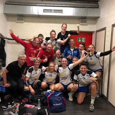 Gruppenfoto von Frauenhandballspielerinnen in Sportkleidung, glücklich nach einem Spiel in einer Umkleidekabine.