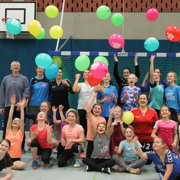 Gruppenspiel mit Jugendlichen in Sportkleidung, die bunte Luftballons in einer Sporthalle werfen und Freude ausstrahlen.