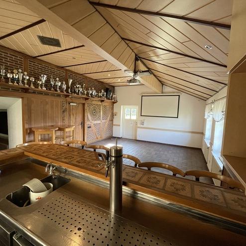 Innenansicht eines Raumes mit Holzdecke, Trophäenwand und Theaterbestuhlung vor einer Leinwand. Bar im Vordergrund.