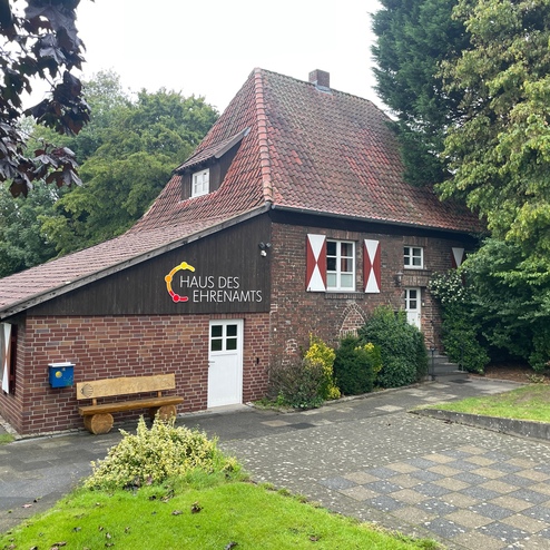 Einfamilienhaus mit rotem Ziegeldach, Holzfassade, weißen Fenstern und der Aufschrift „Haus des Ehrenamts“.