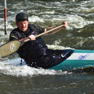 Paddler in einem Kanu kämpft gegen die Strömung eines wildwassergefluteten Flusses. Spritzer um ihn herum.