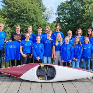 Gruppenfoto einer Kanubauer-Mannschaft in blauen Trikots, posierend neben einem Kanu auf einem Holzsteg.