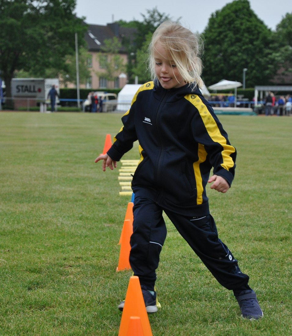 Kind in Sportkleidung balanciert auf einem Parcours aus orangefarbenen Kegeln auf einer Wiese.