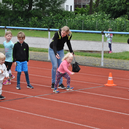 Gruppe von Kindern beim Laufen auf einer roten Tartanbahn, eine Betreuerin hält ein Schild.
