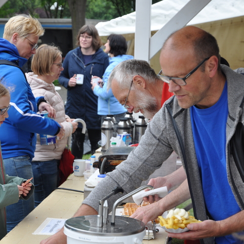 Menschen stehen an einem Essensstand, während ein Mann Waffeln zubereitet und eine Frau Pommes in der Hand hält.