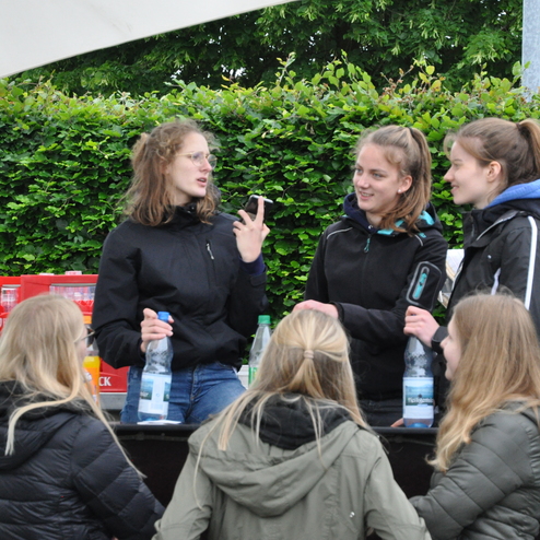 Sechs junge Frauen stehen an einer Getränkebar, während sie miteinander sprechen und Wasserflaschen in der Hand halten.
