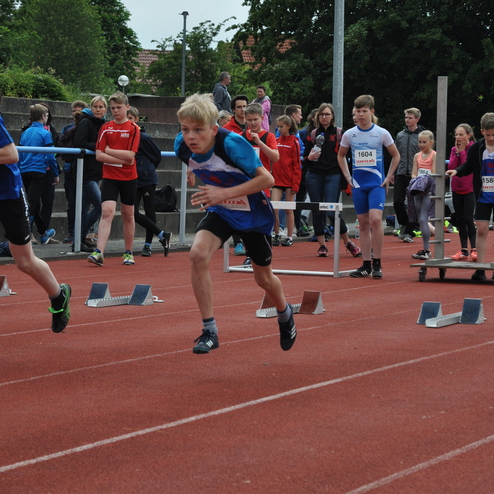 Ein Junge sprintet bei einem Wettkampf über eine Leichtathletikanlage mit Zuschauern im Hintergrund.