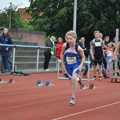 Junger Athlet sprintet auf einer Tartanbahn mit Startblöcken bei einem Wettkampf, im Hintergrund Zuschauer.