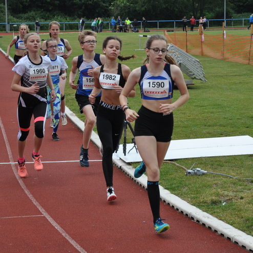 Verschiedene Jugendliche laufen auf einer roten Tartanbahn während eines Wettkampfs im Freien.