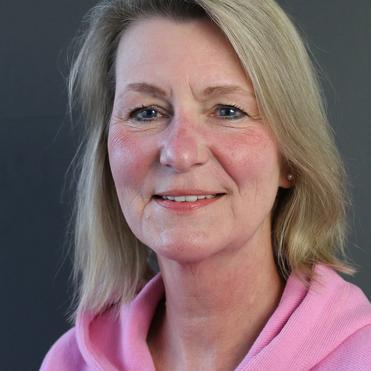 Porträt einer Frau mit blonden, schulterlangen Haaren, die ein pinkes Sweatshirt trägt, vor einem grauen Hintergrund.