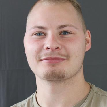 Porträt eines jungen Mannes mit kurzem, blondem Haar und hellblauen Augen, der in die Kamera lächelt. Hintergrund grau.